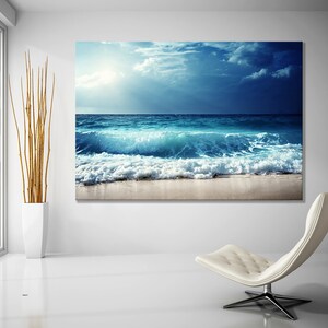 May include: A large canvas print of a blue ocean wave crashing on a sandy beach. The sky is a bright blue with white clouds.