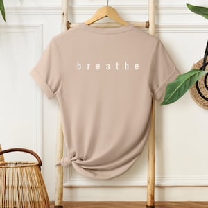 May include: A beige t-shirt with short sleeves and the word "breathe" printed in white on the back.