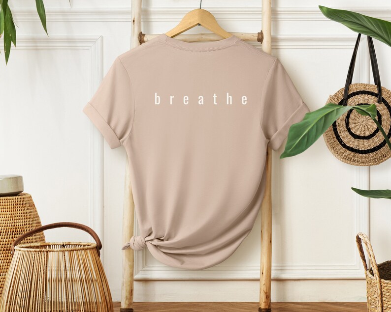May include: A beige t-shirt with short sleeves and the word "breathe" printed in white on the back.
