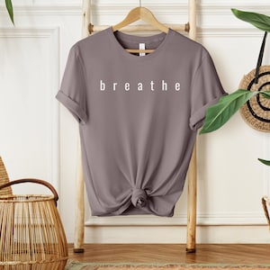May include: A mauve colored t-shirt with the word "breathe" printed in white on the front.