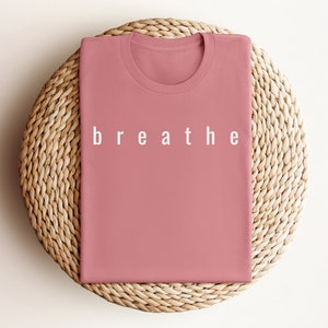 May include: A folded pink t-shirt with the word "breathe" printed in white on the front.