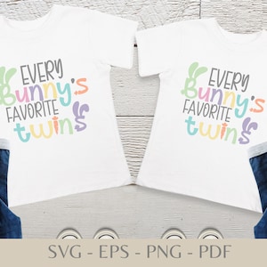 Peut inclure: Deux t-shirts blancs avec le texte "Every Bunny's Favorite Twins" en lettres colorées. Les t-shirts sont sur une surface en bois avec un jean de chaque côté.