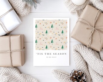 May include: A white card with a green, pink, and yellow patterned design of trees, deer, and flowers. The text "'Tis the season to be jolly" is printed on the card.