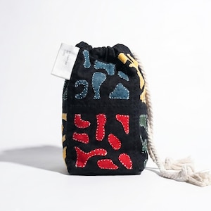 May include: Black drawstring bag with colorful, abstract patchwork designs in red, blue, yellow, and green. The bag has a white drawstring and a small tag. The bag is made of a soft, textured fabric.