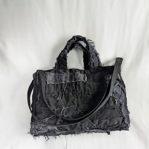 Peut inclure: Sac fourre-tout noir en patchwork avec une bandoulière et deux poignées. Le sac est fait de tissu denim avec des bords effilochés et des coutures visibles. Le sac est de forme rectangulaire.
