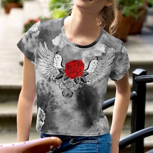 Könnte beinhalten: Graues Crop-Top mit einem Design im Aquarellstil. Das Shirt zeigt eine rote Rose mit weißen Flügeln und schwarzen Akzenten. Das Oberteil ist kurzärmlig und hat einen runden Ausschnitt.