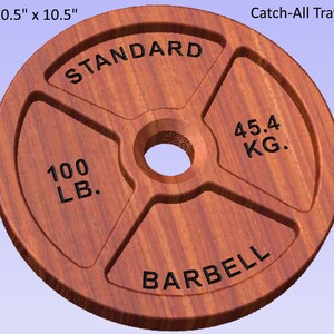 May include: A wooden weight plate with a brown wood grain finish. The plate is 10.5 inches in diameter and has the text "STANDARD", "100 LB.", "45.4 KG.", and "BARBELL" engraved on it. The plate is designed to be used as a catch-all tray.