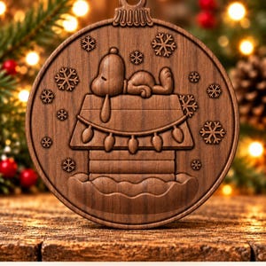 May include: A circular wooden ornament featuring a carved design of a dog sleeping on top of a doghouse decorated with string lights and surrounded by snowflakes. The text Digital CNC File - No Physical Product is printed below.