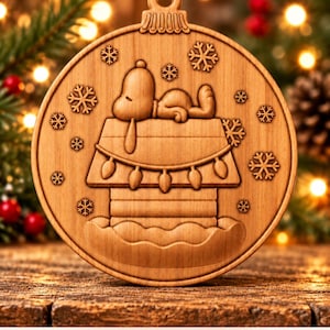 May include: A round wooden Christmas ornament featuring a carved design of a dog sleeping on top of a doghouse with string lights and snowflakes. The text Digital CNC File - No Physical Product is printed at the bottom of the image.