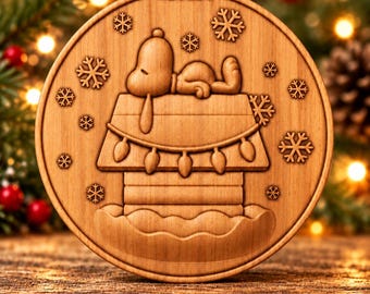 May include: A round wooden Christmas ornament featuring a carved design of a dog sleeping on top of a doghouse with string lights and snowflakes. The text Digital CNC File - No Physical Product is printed at the bottom of the image.