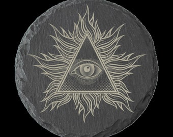 Puede incluir: Un posavasos de pizarra negra con un diseño de ojo que todo lo ve en blanco. El ojo está dentro de un triángulo con un patrón de sol radiante.