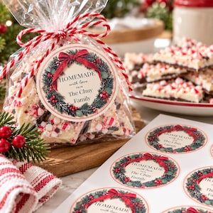 Puede incluir: Una bolsa de plástico transparente llena de corteza de chocolate y menta, atada con cordel rojo y blanco. Una pegatina redonda muestra una corona verde con un lazo rojo y el texto: HOMEMADE with love FROM The Chuy Family.