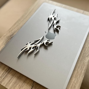 Può includere: Un laptop argentato con un design in metallo decorativo sul coperchio. Il laptop è appoggiato su una superficie in legno.