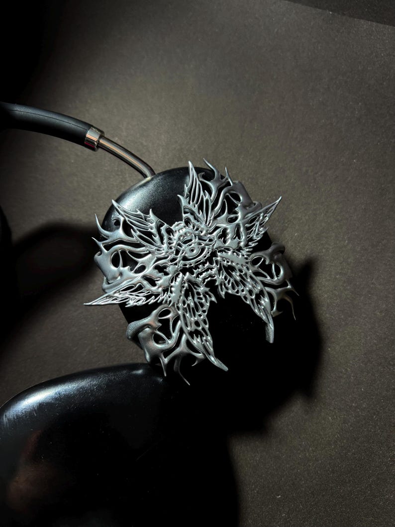 May include: Silver headphone earcup with a detailed, intricate, and ornate design of a stylized butterfly with a central eye.
