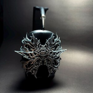 May include: Black headphones with a silver, intricate, butterfly-shaped design on the earcups.