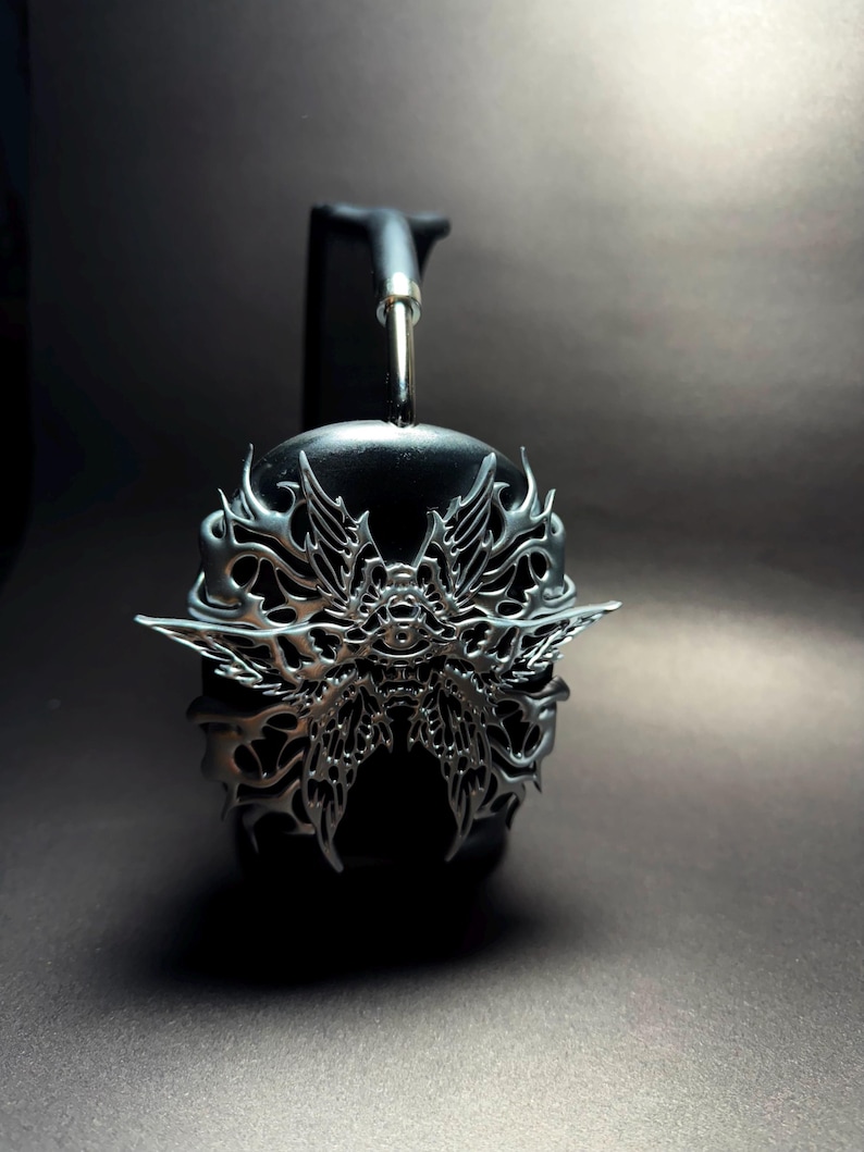 May include: Black headphones with a silver, intricate, butterfly-shaped design on the earcups.
