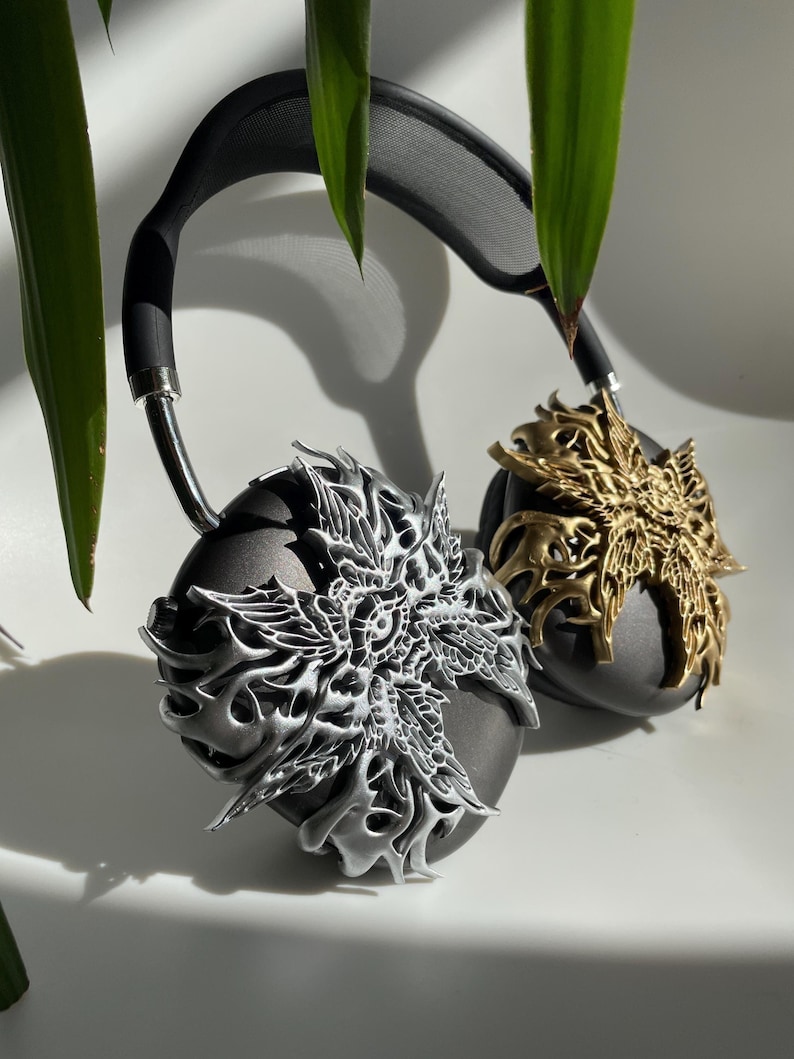 May include: A pair of black headphones with silver and gold decorative earcups. The earcups feature intricate, detailed designs.