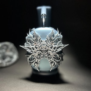 May include: A silver-coloured headphone accessory with a detailed, intricate design resembling a butterfly. The accessory is attached to a light blue headphone.