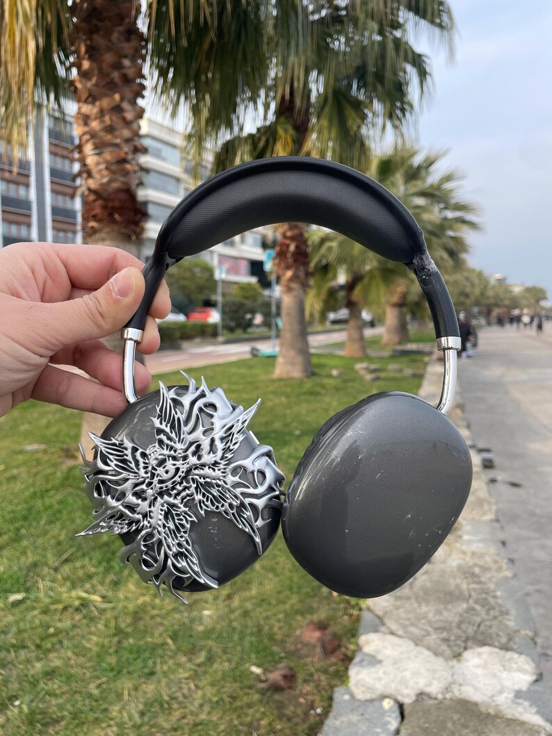 May include: A pair of black headphones with a silver decorative design on one earcup. The headphones have a black headband and a silver metal frame.