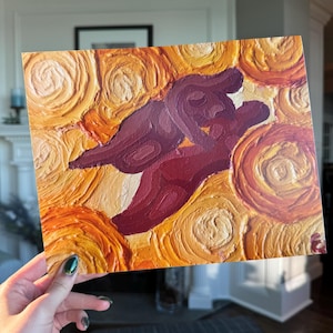 May include: An abstract painting with a textured, impasto style. The artwork features swirling patterns in shades of orange and yellow, surrounding a central form in deep burgundy. The painting is held by a person.