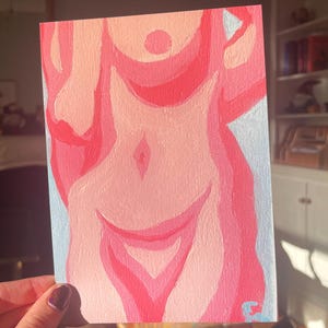 May include: A pink and red abstract painting of a torso on a light blue background. The artwork features layered shades of pink and red, with a focus on the form and shape of the body. The painting is held by a hand.