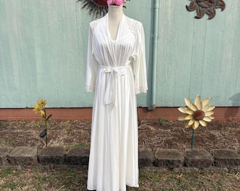 May include: A white vintage robe and nightgown set displayed on a mannequin. The robe has long sleeves, lace trim, and a tie waist. The nightgown is visible underneath. The background features a light blue wall and decorative metal suns.