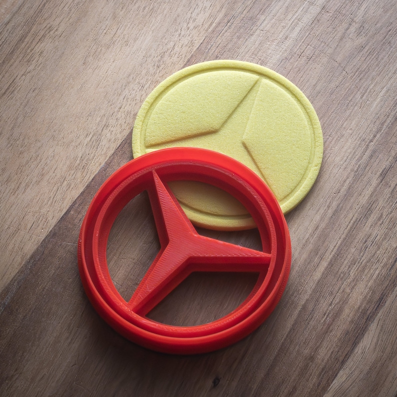 May include: A red plastic cookie cutter shaped like a three-pointed star, with a yellow plastic cookie cutter on top of it.