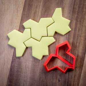 Könnte beinhalten: Ein Satz von fünf gelben sternförmigen Ausstechern und ein roter Ausstecher in Form eines stilisierten Buchstabens T. Die Ausstecher befinden sich auf einer Holzoberfläche.