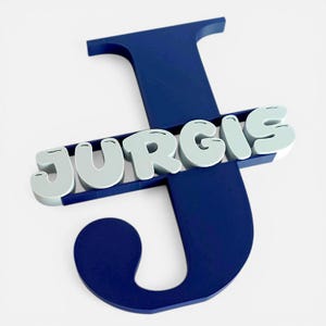 Puede incluir: Una letra "J" de madera azul marino con el nombre "Jurgis" en letras 3D de color gris claro. El nombre se coloca horizontalmente sobre la letra "J". Esta decoración de pared personalizada es adecuada para la habitación de un niño o guardería.