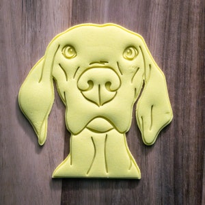 Op de afbeelding: Een gele rubberen sjabloon van een hondenkop. De hond heeft slappe oren en een lange snuit.
