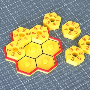 May include: A yellow and red number puzzle game with hexagonal pieces. Each piece has a hole in the center and numbers around the edges. The game is designed to fit together, with the pieces forming a larger honeycomb shape.