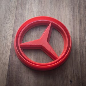 May include: A red plastic cookie cutter shaped like the Mercedes-Benz logo.