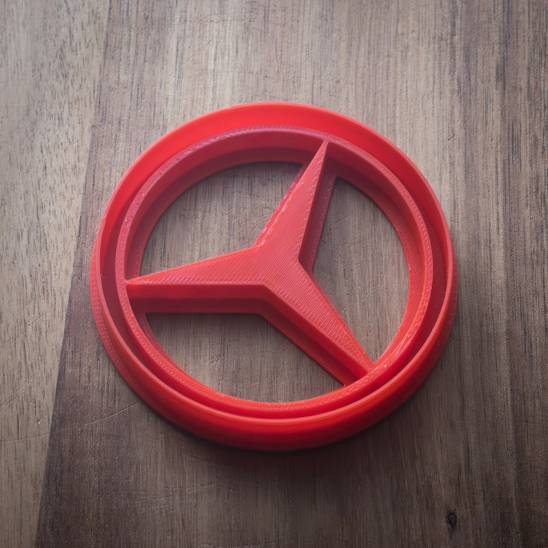 May include: A red plastic cookie cutter shaped like the Mercedes-Benz logo.