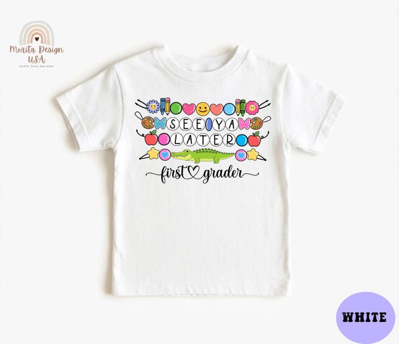 May include: White t-shirt with a colorful graphic that says "SEE YA LATER" with a crocodile and the words "first grader". The design includes various school-themed elements like pencils, apples, and stars.