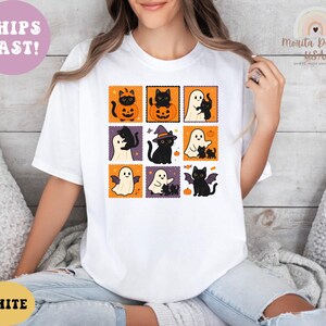 May include: White t-shirt featuring a grid of Halloween-themed illustrations. Each square showcases a black cat, ghost, or bat with pumpkins and witch hats. The shirt has the text "WHITE" and "SHIPS FAST!"