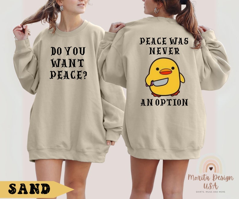 K&ouml;nnte beinhalten: Ein beiger Pullover mit dem Text "Do you want peace?" auf der Vorderseite und "Peace was never an option" mit einem Cartoon-gelben K&uuml;ken, das ein Messer h&auml;lt, auf der R&uuml;ckseite.