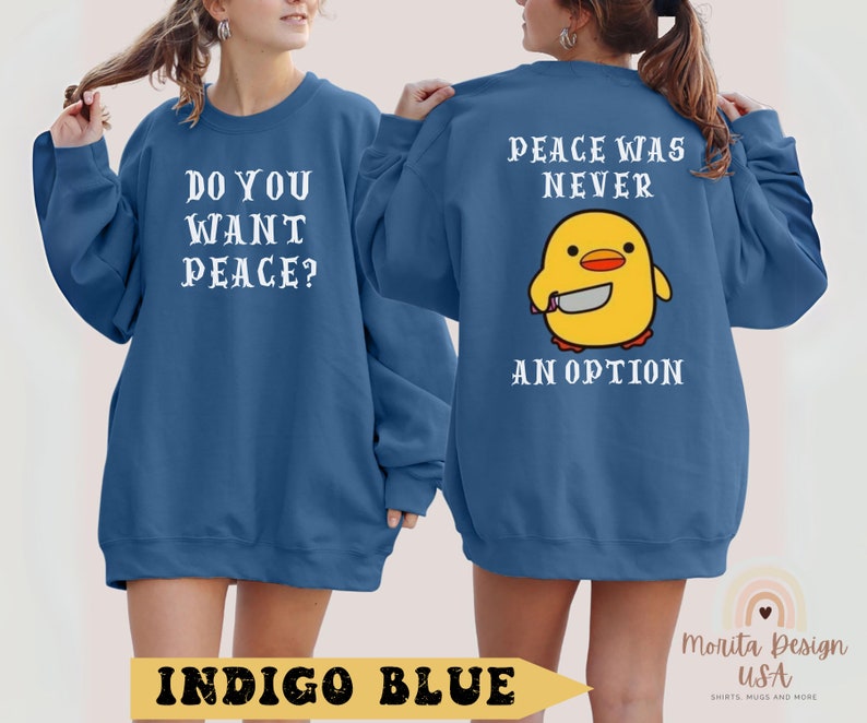 K&ouml;nnte beinhalten: Zwei indigo-blaue Sweatshirts mit wei&szlig;em Text. Ein Sweatshirt sagt "Willst du Frieden?" und das andere sagt "Frieden war nie eine Option." Beide Sweatshirts zeigen ein Cartoon-gelbes K&uuml;ken, das ein Messer h&auml;lt.