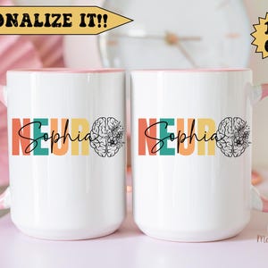 Op de afbeelding: Twee witte 440 ml mokken met roze handvatten. De mokken hebben een kleurrijk ontwerp met het woord "Neuro" en de naam "Sophia" in een regenboog-lettertype. Aan de rechterkant van elke mok staat een brein met bloemen.