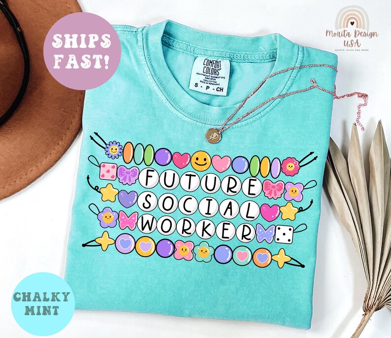 May include: A turquoise t-shirt with the words "FUTURE SOCIAL WORKER" in white letters, surrounded by colorful beads and decorative elements. The shirt has a crew neck and short sleeves. A gold necklace is draped across the shirt.