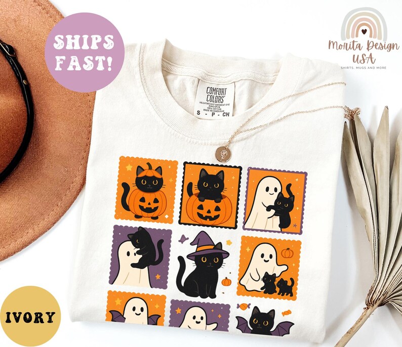 May include: Ivory-colored t-shirt featuring a Halloween-themed design. The design includes black cats, ghosts, pumpkins, and bats in a postage stamp style. The shirt also has the text "Comfort Colors" and "S P CH".