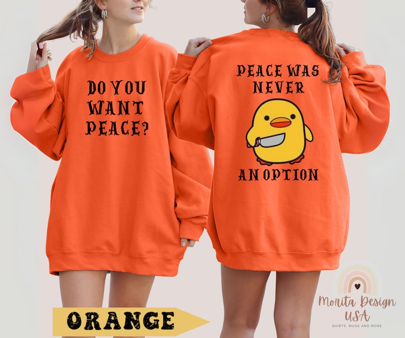 K&ouml;nnte beinhalten: Orangefarbener Pullover mit dem Text "Do you want peace?" auf der Vorderseite und "Peace was never an option" mit einem Cartoon-K&uuml;ken, das ein Messer h&auml;lt, auf der R&uuml;ckseite.