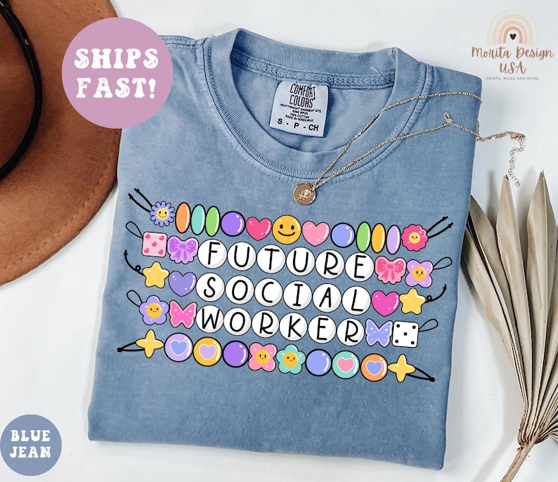 May include: A blue jean Comfort Colors t-shirt with the text "FUTURE SOCIAL WORKER" in white, surrounded by colorful beaded accents. The shirt has a crew neck and short sleeves. A gold necklace is draped across the shirt.
