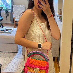 May include: A colorful crocheted handbag with a pink, orange, yellow, purple, and green design. The bag has a gold clasp and a tassel.