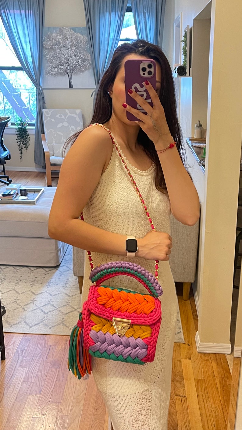 May include: A colorful crocheted handbag with a pink, orange, yellow, purple, and green design. The bag has a gold clasp and a tassel.