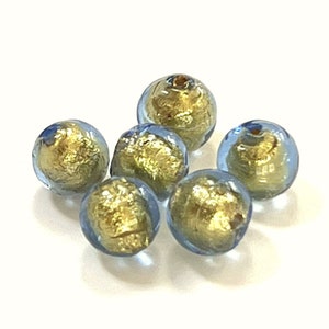May include: Six round glass beads with a light blue color and gold flecks. The beads are scattered on a white surface.