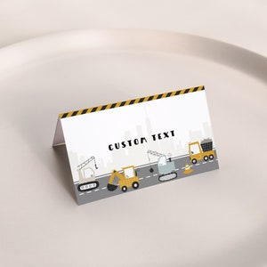 Könnte beinhalten: Konstruktionsthemen-Platzkarte mit gelbem und schwarzem Streifenrand. Die Karte zeigt eine Skyline der Stadt mit Baufahrzeugen, darunter ein Kran, ein Bulldozer und ein Kipplaster. Der Text "CUSTOM TEXT" ist auf die Karte gedruckt.
