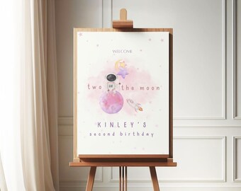 May include: A white welcome sign with pink watercolor clouds and stars. The text reads "Welcome to the moon, Kinley's second birthday".