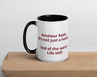 May include: White ceramic mug with a black handle and interior. The mug features the text "Amateur Radio (it's not just a hobby) End of the world Life skill" in maroon lettering. The mug is sitting on a wooden surface.