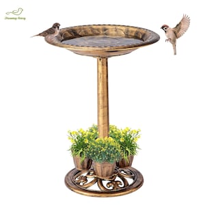 May include: Bronze-colored bird bath with a decorative rim, supported by a tall, slender post. The base features a circular design with three small potted plants with yellow flowers. Two birds are perched on the bird bath.