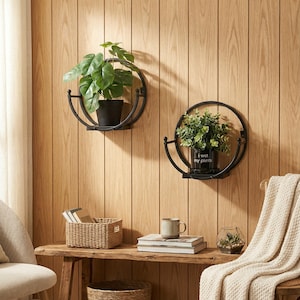 Puede incluir: Dos estantes de pared circulares de metal negro con plantas. Uno de los estantes contiene una planta en maceta con hojas verdes grandes. El otro estante contiene una planta en una maceta con el texto "I wet my plants". Los estantes están montados en una pared de madera.
